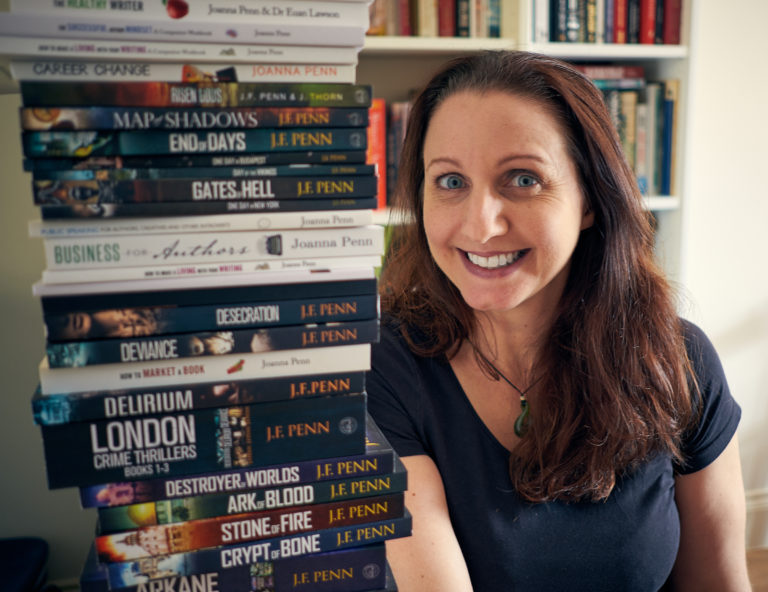 A photo of Joanna Penn seated beside a giant stack of her books.